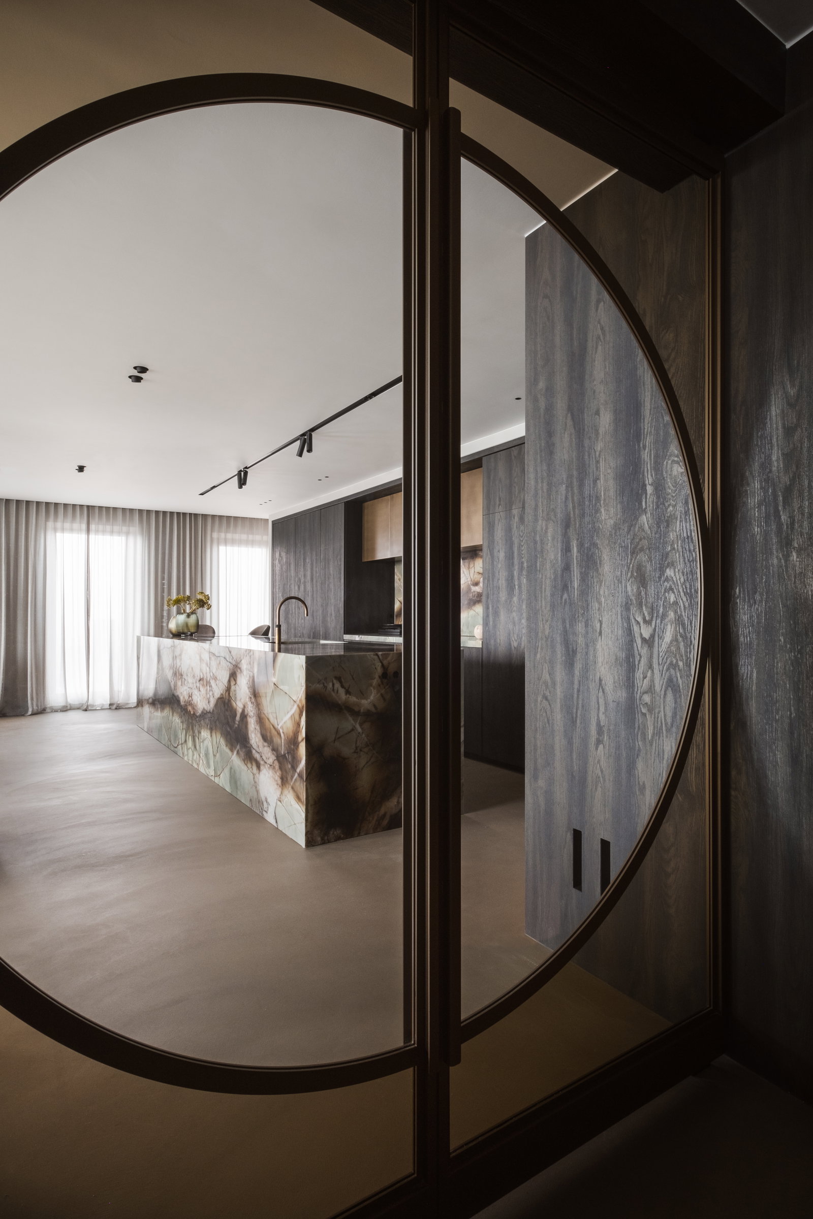 Round glass pivot door open to an apartment with a marble kitchen island, Zalmhaventoren, with FritsJurgens System M+ pivot hinge inside