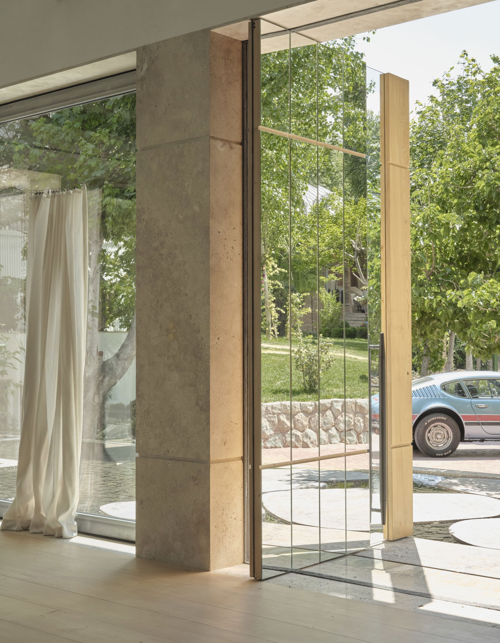 A European oak pivot door with integrated glass and mirror panels, offering a sculptural experience over serene waters.