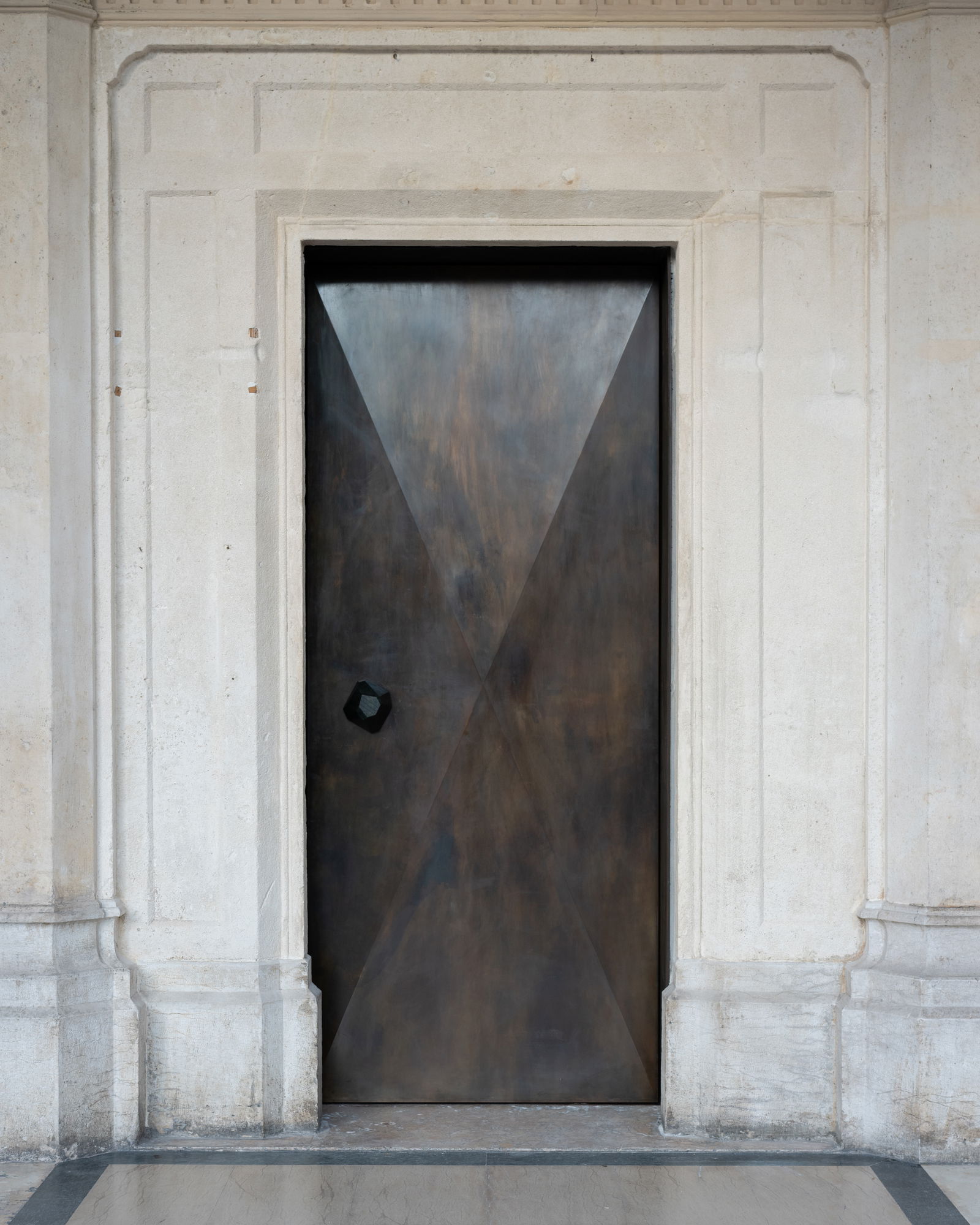 A burnished steel, diamond-shaped door merging historical memory with contemporary precision.