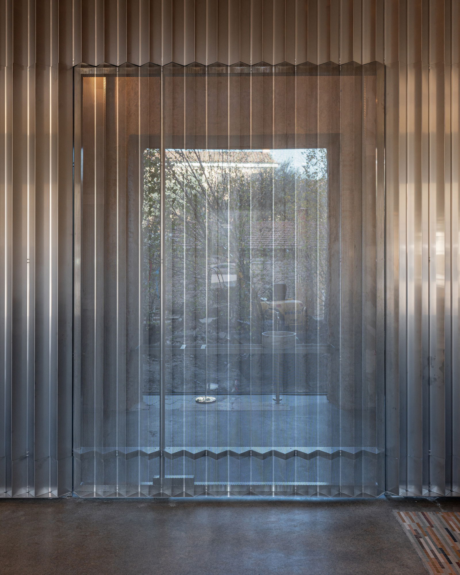 A micro-perforated stainless steel pivoting panel integrated seamlessly into an undulating wall.