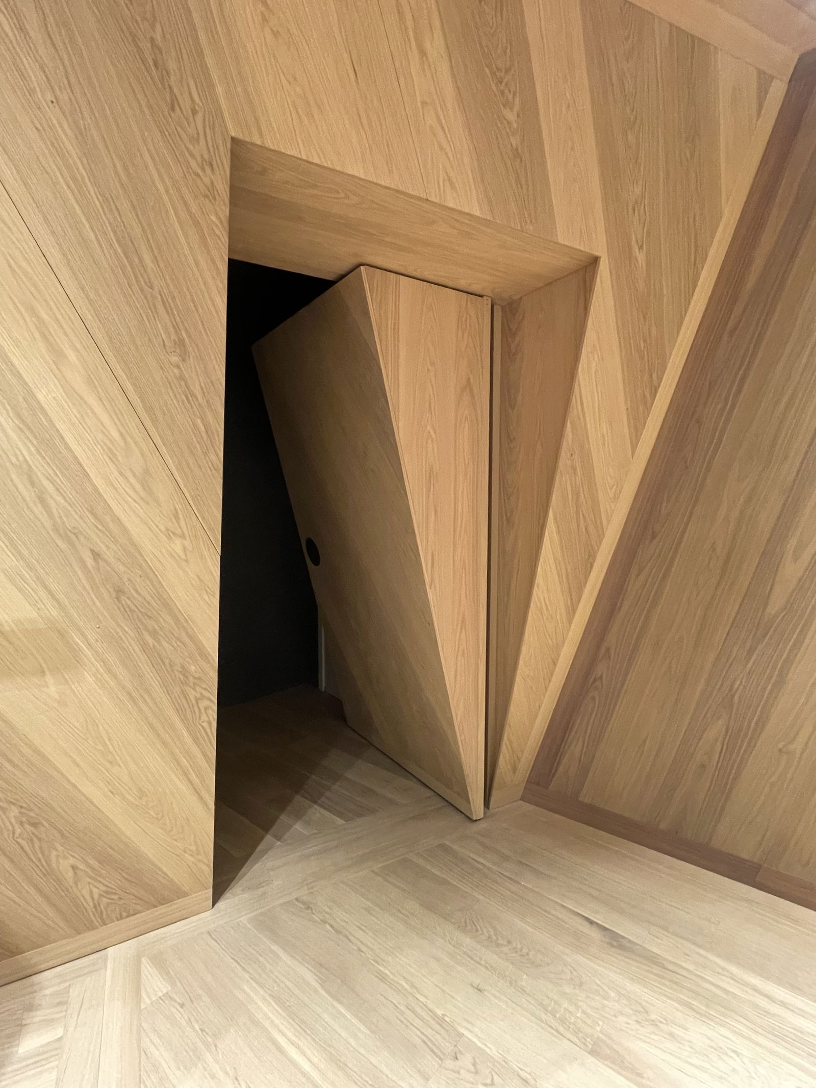 An angled oak veneered wall conceals a pivot door with variable thickness for flawless integration.