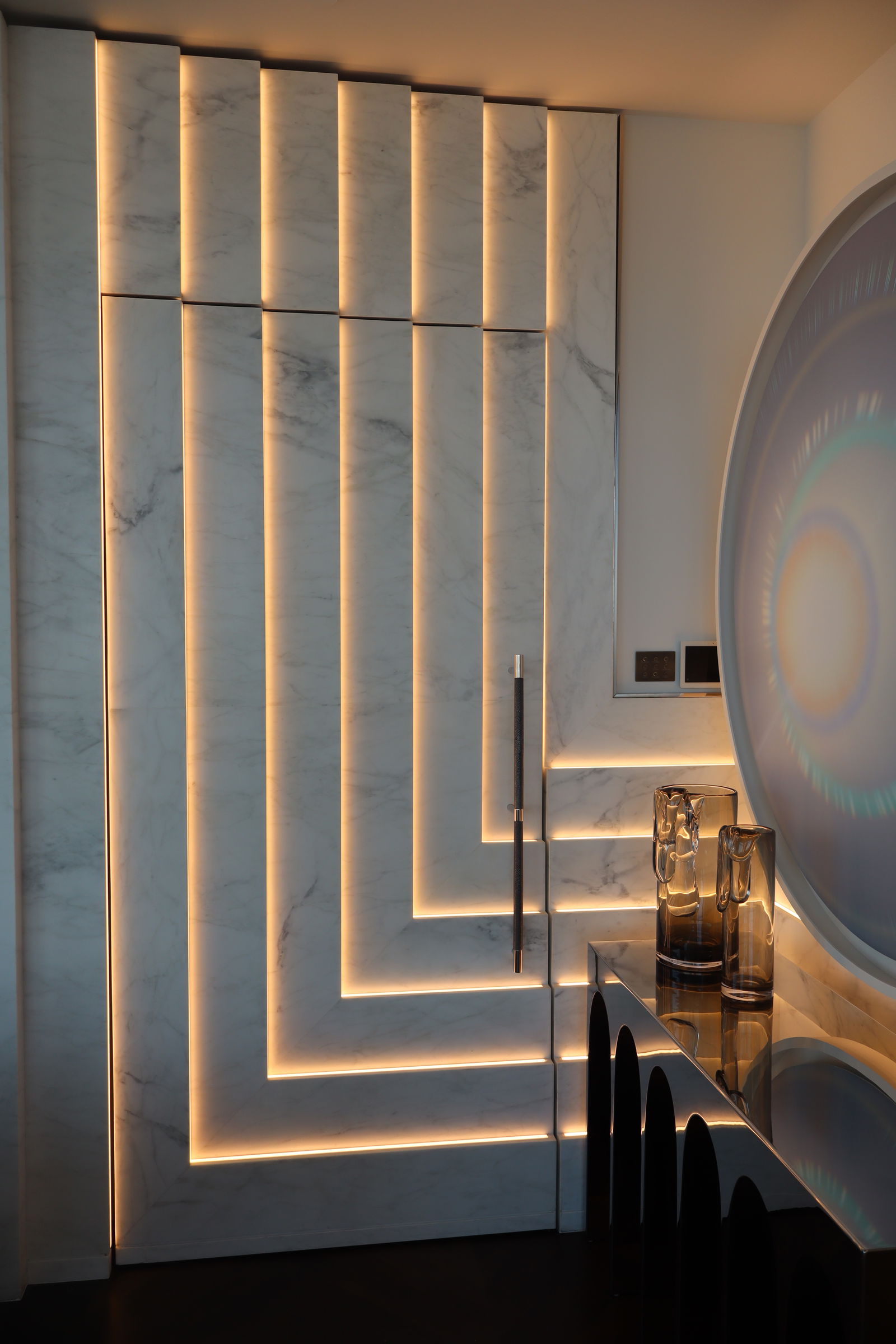 A sculptural pivot door crafted from polished metal, marble, speciality glass, and LEDs.